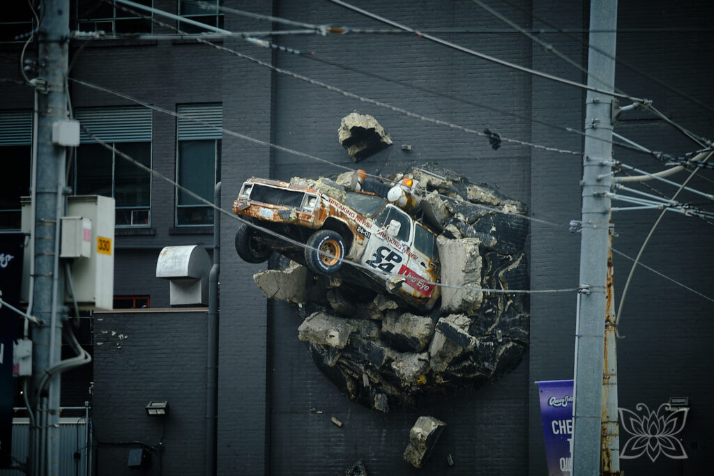 Ein Auto ist an einer Fassade so angebracht, dass es aussieht, als durchbreche es die Wand