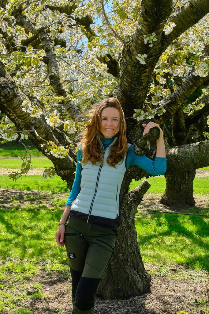 Coach Inga Noetel an Baum in Frühlingsblüte gelehnt