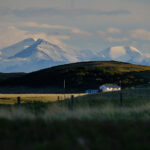 Inga Noetel auf Weltreise - Verschneite Rocky Mountains in Kanadas Westen mit Farmhaus und hügeliger Graslandschaft im Vordergrund