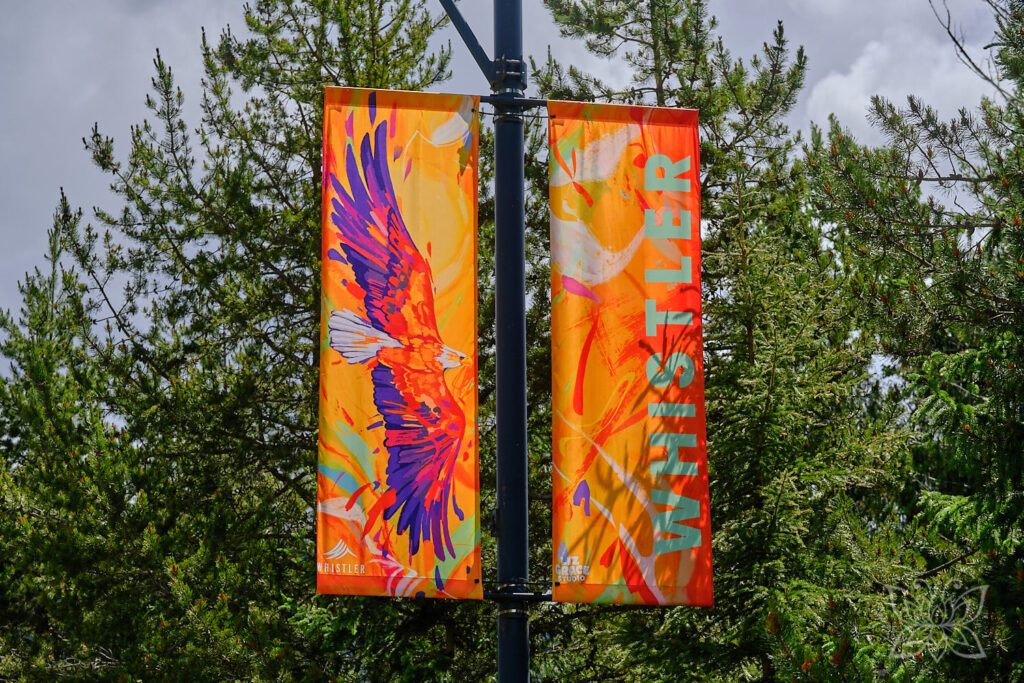Orange-bunte Fahnen mit Schriftzug der Stadt und einem fliegenden Adler-Motiv heißen Gäste in Whistler herzlich Willkommen