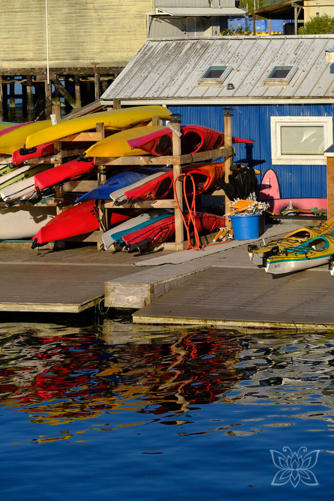 Bunte Kanus an einem Bootshaus reflektieren sich im Wasser