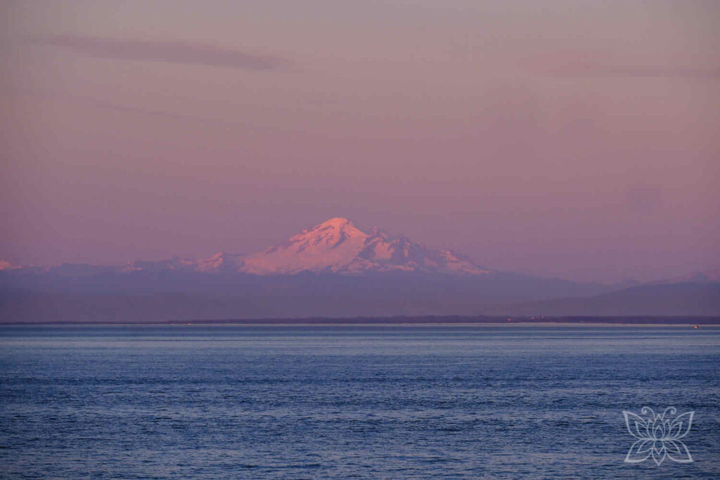 Schneebedeckte Bergkuppe im Hintergrund einer Bucht in der Abenddämmerung