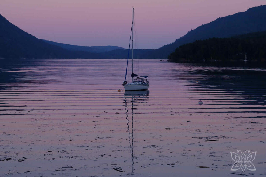 Segelboot in einer von Hügeln umschlossenen Bucht in der Abenddämmerung. 